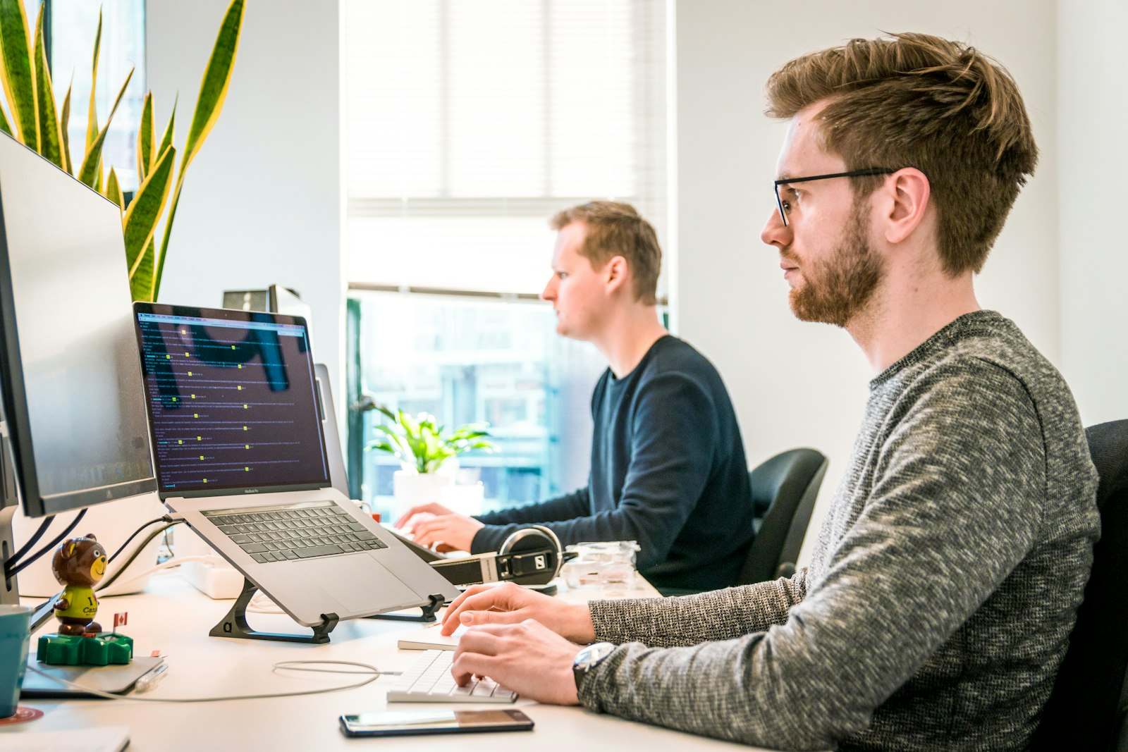 Dwóch pracowników przy biurkach z laptopami w jasnym biurze