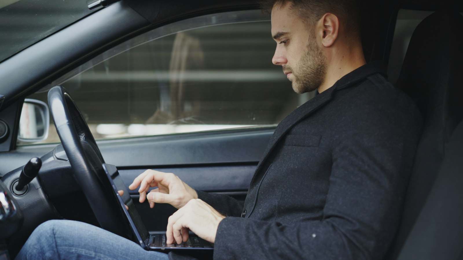 Mężczyzna w marynarce pracuje na laptopie w zaparkowanym samochodzie