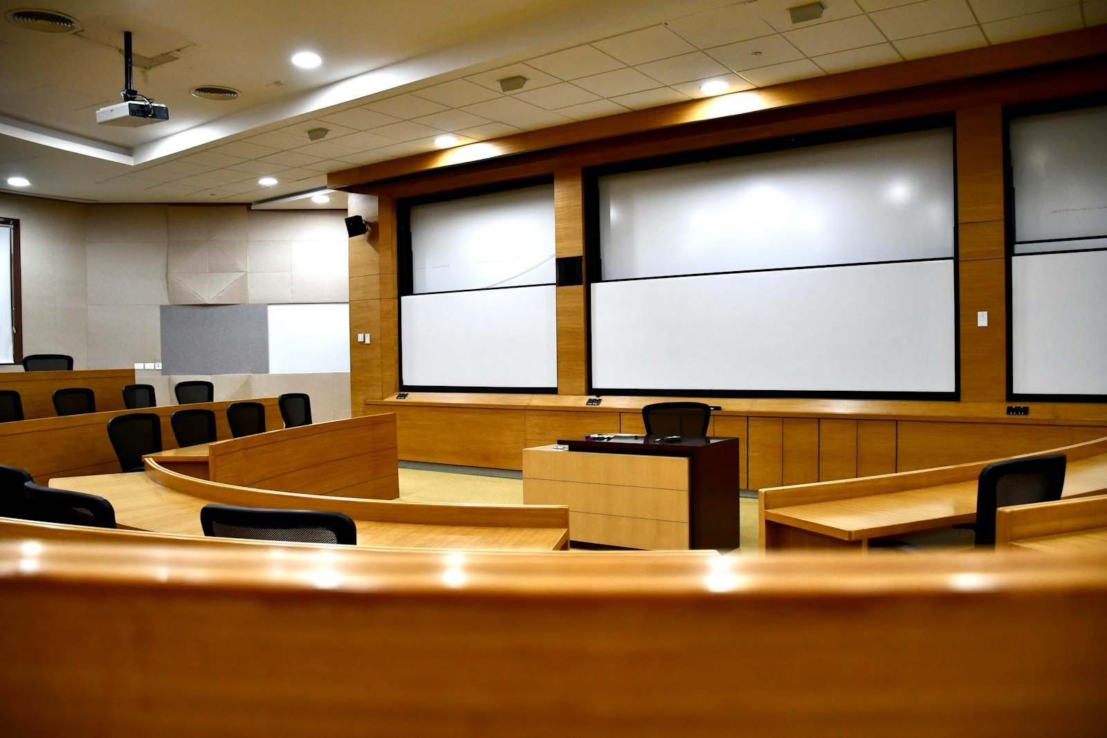 Pusta sala wykładowa z ekranami projekcyjnymi i drewnianymi ławkami